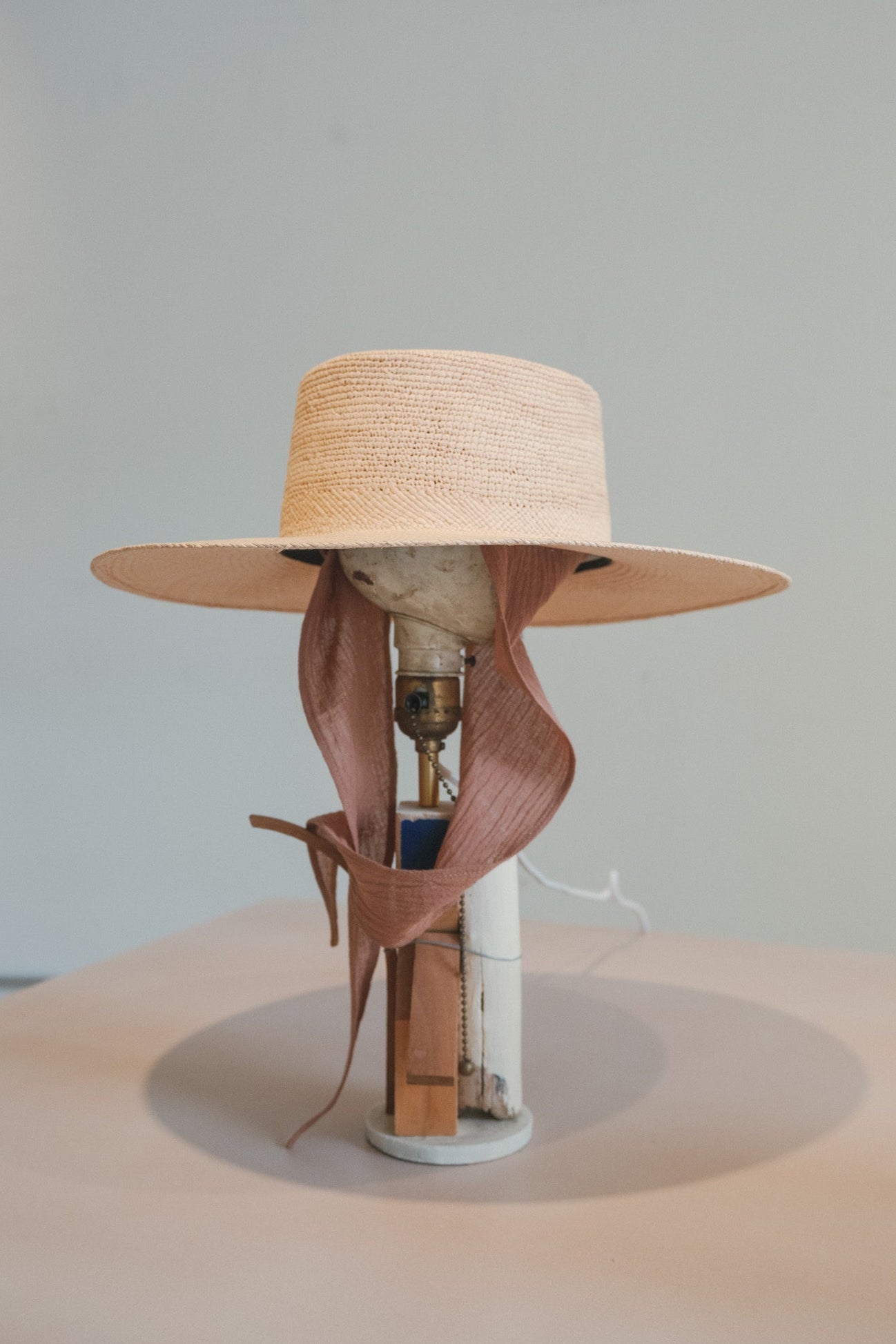 Lamp with a straw hat and ribbon on a neutral background