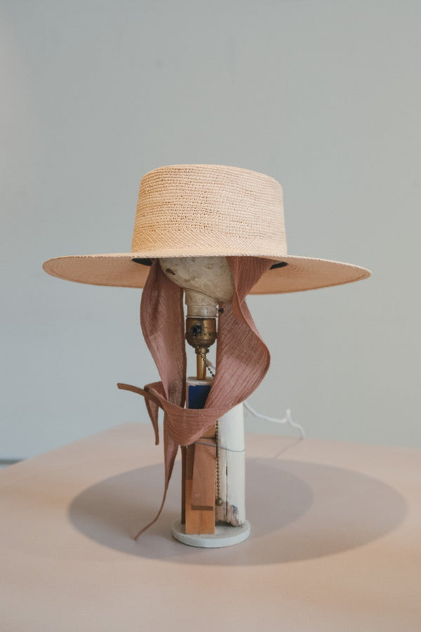 Lamp with a straw hat and ribbon on a neutral background