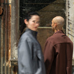 Two people standing in front of a rusty corrugated metal wall.