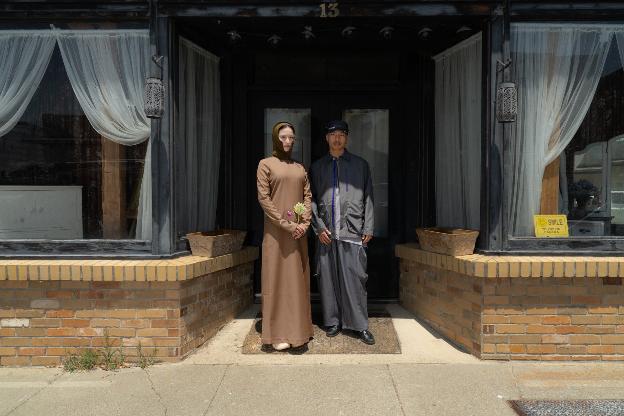 Two people standing outside a building with large windows and curtains.