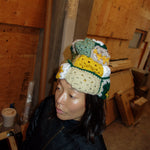 Woman wearing crocheted beanie in mustard yellow / green / white / beige