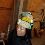 Woman wearing crocheted beanie in mustard yellow / green / white / beige