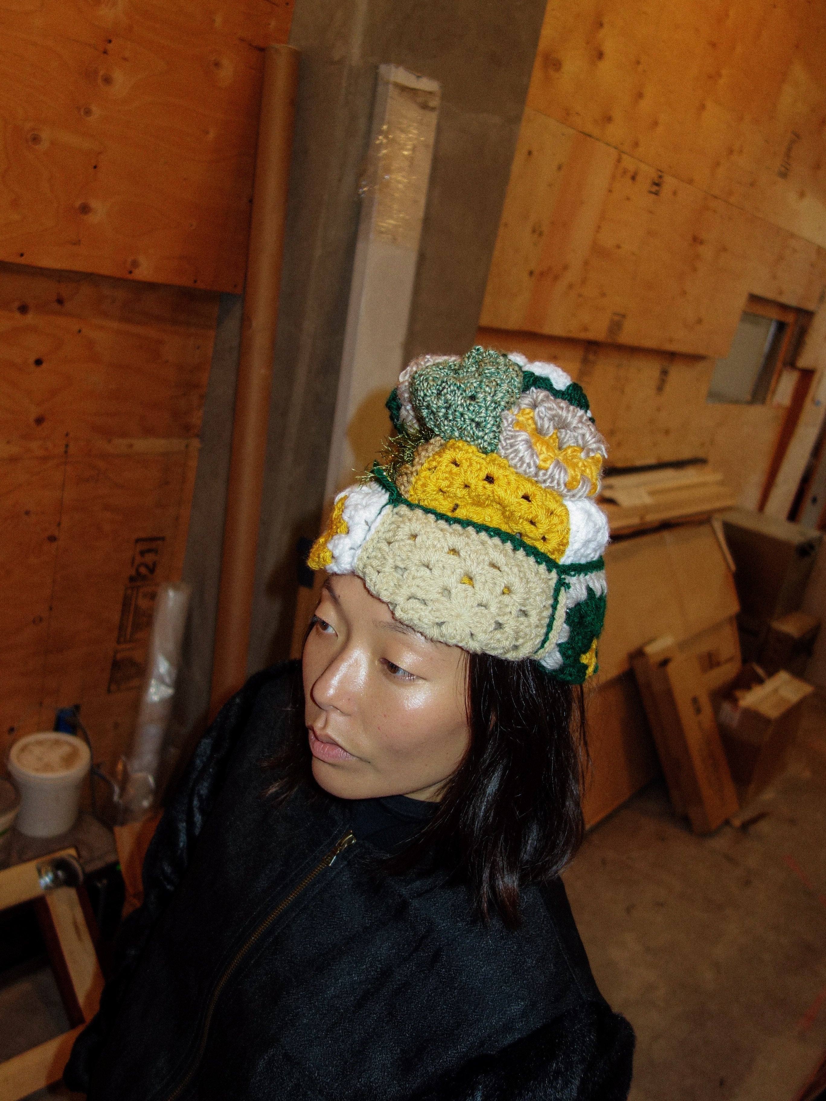 Woman wearing crocheted beanie in mustard yellow / green / white / beige